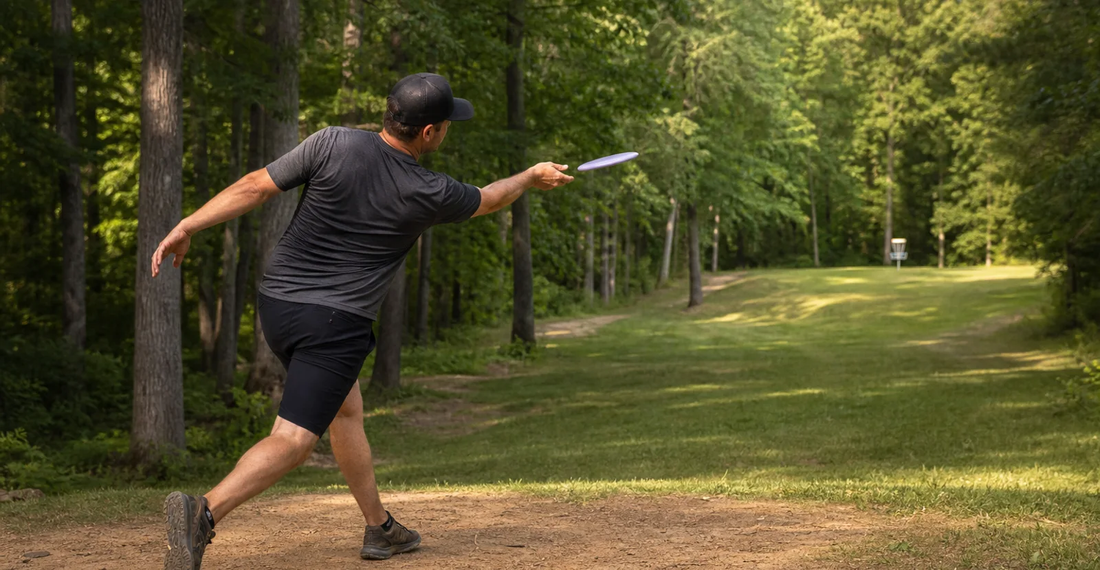 Disc golfer releasing a right-hand backhand anhyzer shot on a wooded fairway