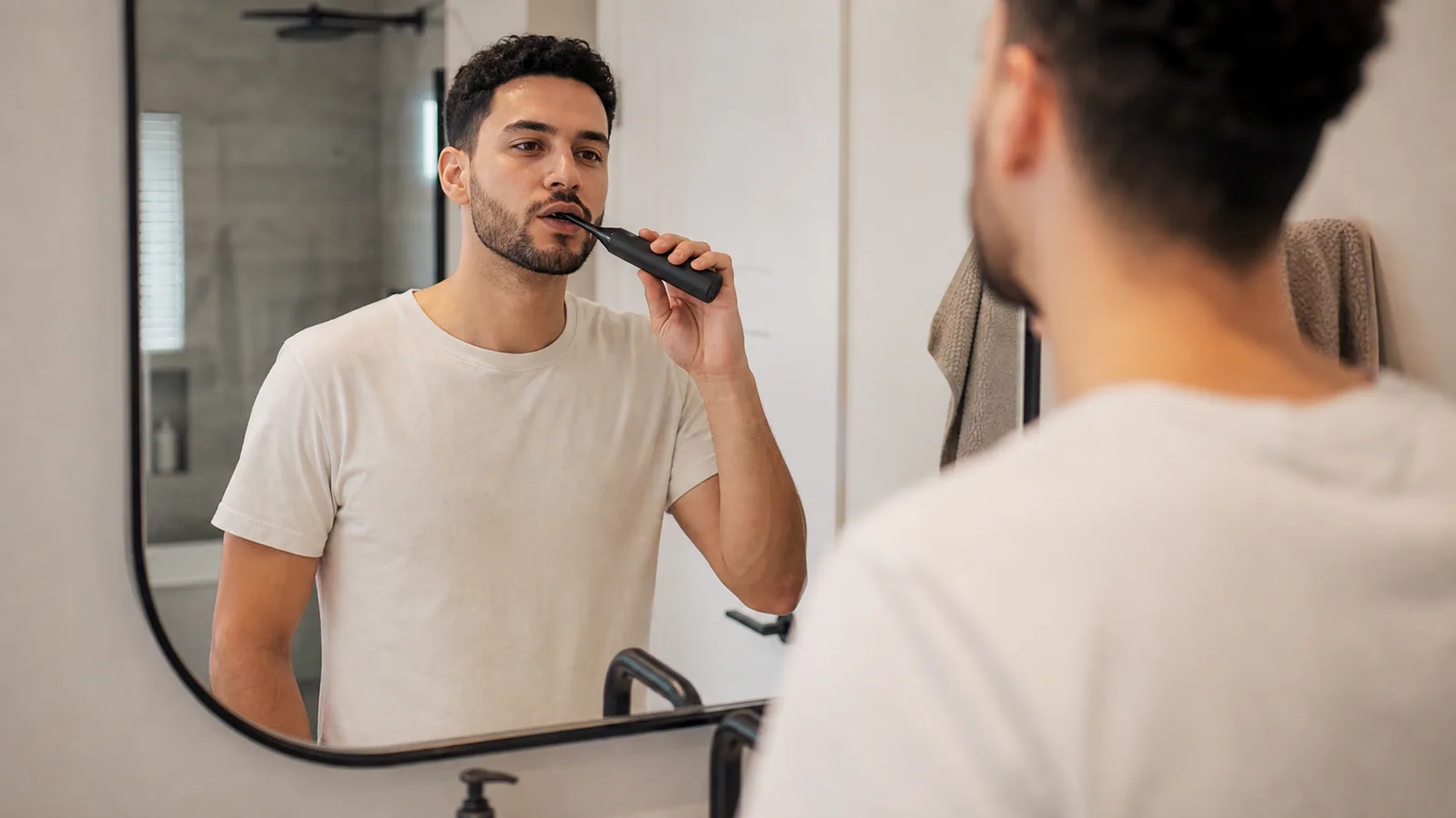 Person using an electric toothbrush during a simple morning bathroom routine