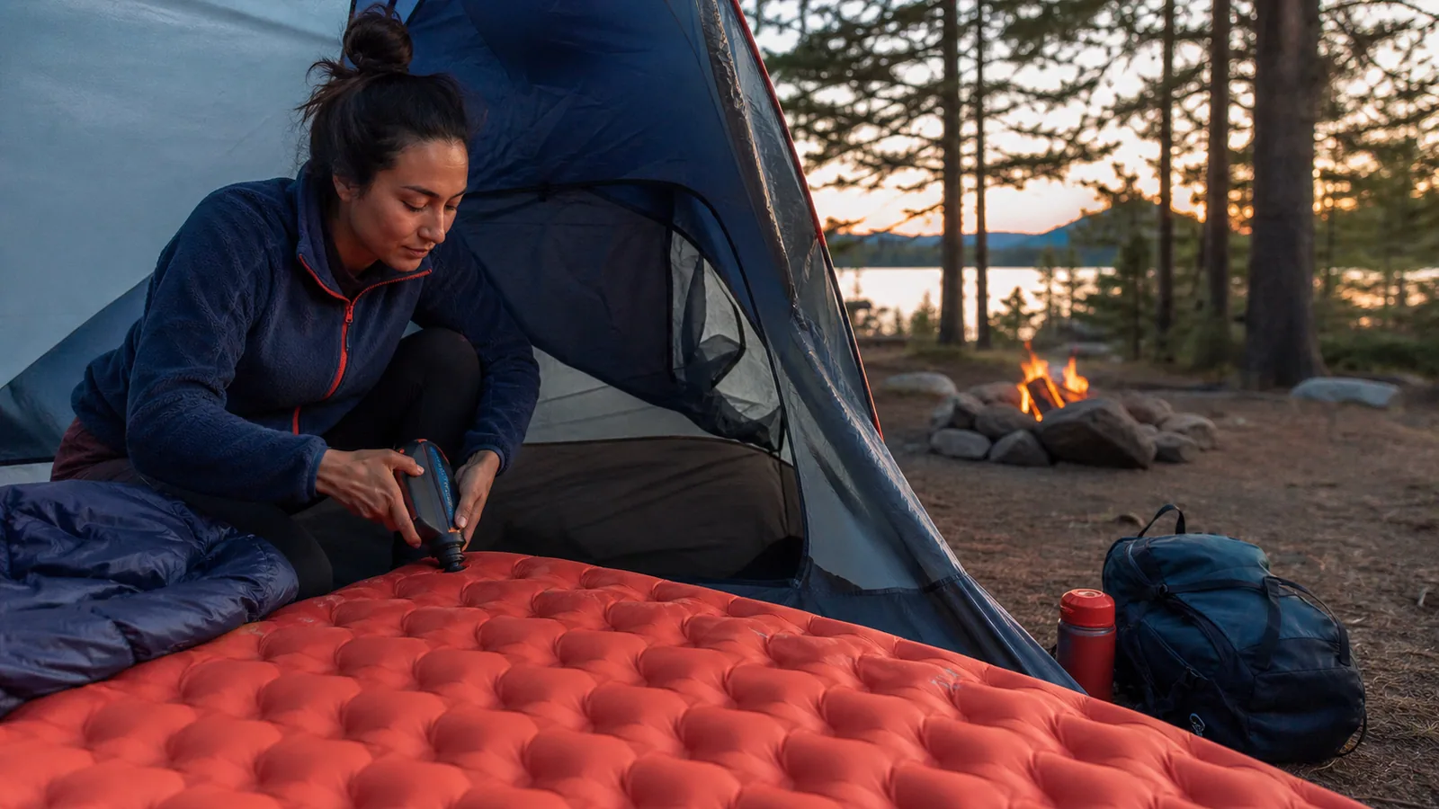 Camper inflating a sleeping pad inside a tent at dusk
